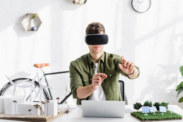 arquiteto em fone de ouvido de realidade virtual à mesa com laptop e modelos no escritório
 - Foto, Imagem