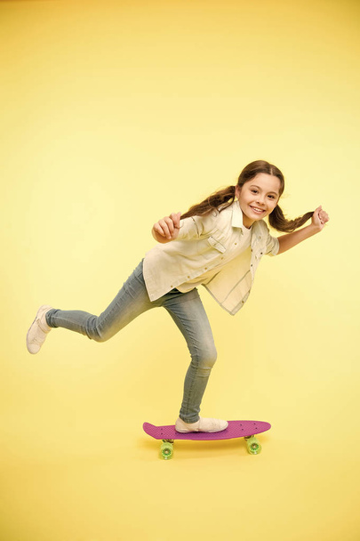 Girl ride penny board yellow background. Kid having fun with penny board. Carefree happy ride. Hobby favorite activity from childhood. Young generation hobby. Child smiling face stand on skateboard - 写真・画像