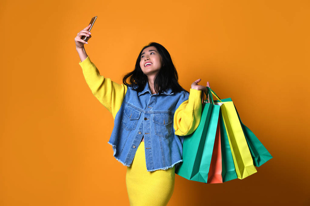 Young asian woman with shopping bags on color background - Valokuva, kuva