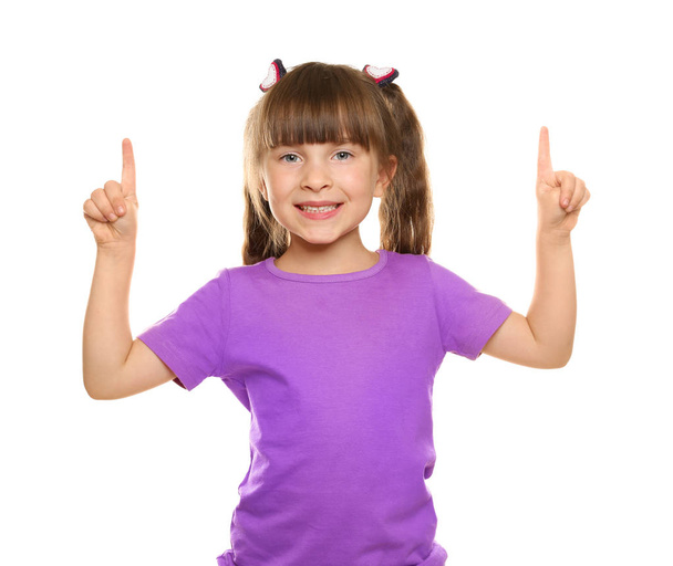 Little girl in t-shirt pointing at something on white background - Photo, Image