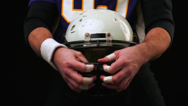 American football. American football player holds helmet with both hands. A big american football player. Preparing for the game. Training. Close-up, black background - Footage, Video
