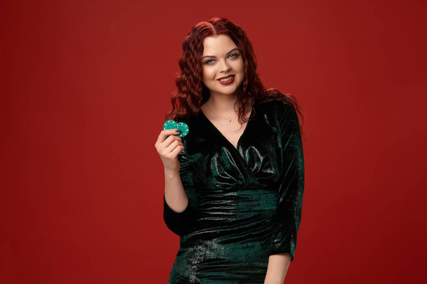 Lucky redheaded woman holding a blue gambling chips in her hands on a red background. - Foto, immagini