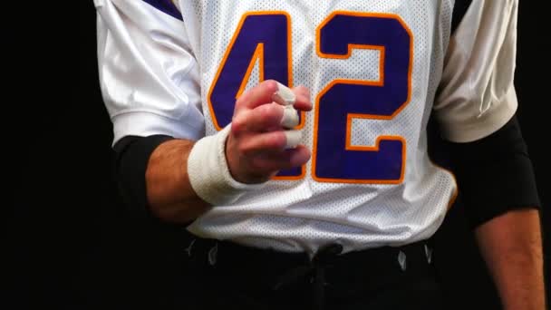 American football player clenching his fist before a big event, giving the impression of tension, concentration or build-up. close up and straight on a black background. - Footage, Video