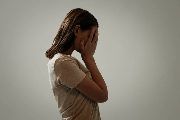 Porträt einer depressiven Frau, das Gesicht mit den Händen verdeckt, Seitenansicht - Foto, Bild
