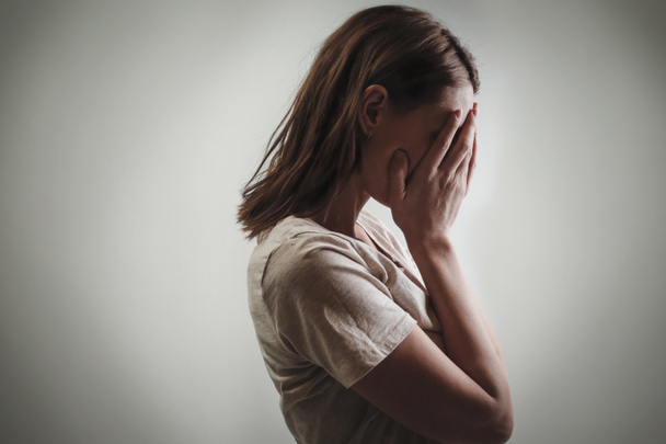 Porträt einer depressiven Frau, das Gesicht mit den Händen verdeckt, Seitenansicht - Foto, Bild