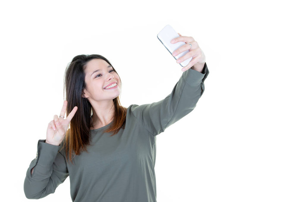 Fashion cool girl taking picture selfie portrait on smartphone making peace sign over white background - Foto, afbeelding