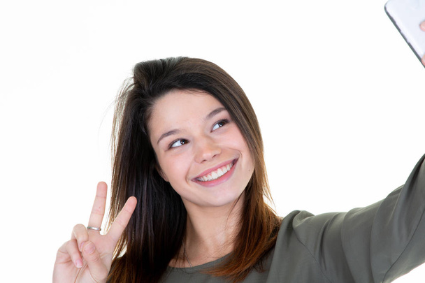 young smiling woman taking a selfie with smartphone making peace sign - Foto, Imagen