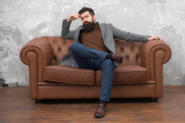 Loft interior apartment. Businessman realtor work. Furniture shop. Hipster realtor loft style apartment. Realtor and rental service. Rent apartment. Bearded man with confident face sit leather couch - Zdjęcie, obraz