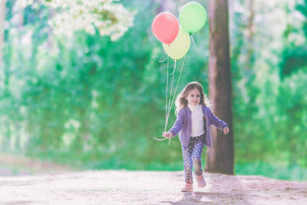 A smiling little girl runs with balloons in their hands. On the background of green forest. - Fotografie, Obrázek