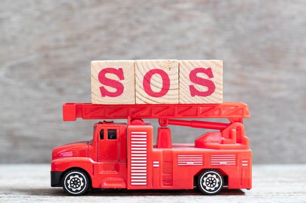 Red fire truck przytrzymaj literę bloku w słowo Sos (skrót od zapisać naszej duszy/statku lub równorzędny przez ramię) na tle drewna - Zdjęcie, obraz