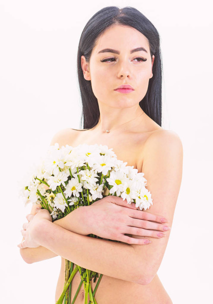 Girl on calm face naked holds chamomile flowers in front of breasts. Natural cosmetics concept. Woman with smooth healthy skin looks attractive. Lady covers breasts with flowers, isolated on white - Photo, Image