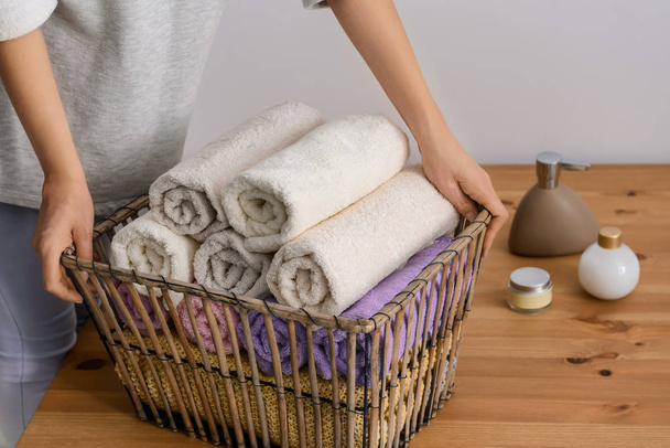 Woman folding clean soft towels into basket at wooden table - Foto, Imagen