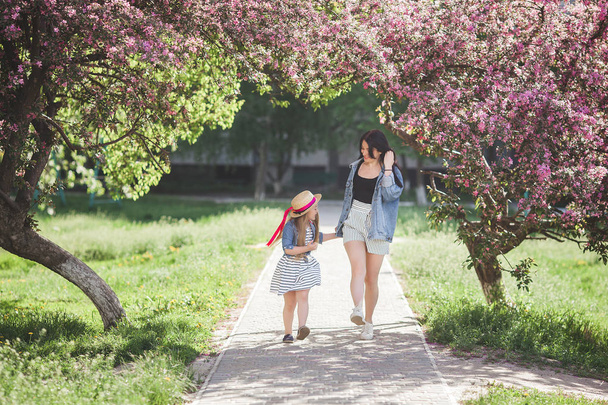 Jonge aantrekkelijke moeder en haar dochtertje plezier samen op lente achtergrond. Meisjes in bloemen. Familie buitenshuis. Zomer stemming. - Foto, afbeelding