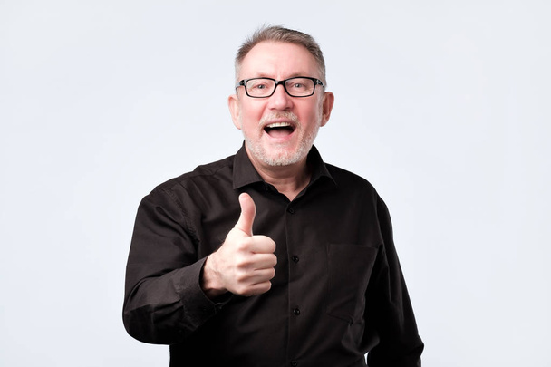 Senior gutaussehender Mann in schwarzem Hemd und Brille zeigt Daumen hoch Geste - Foto, Bild