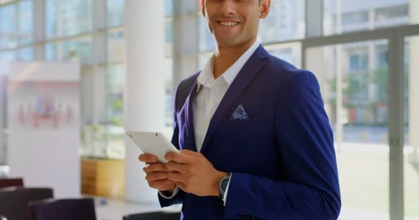 Front view of a mixed-race businessman holding a digital tablet while smiling and looking at camera in the lobby at office 4k - Кадры, видео