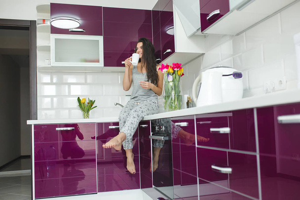 Красивая молодая женщина на новой кухне. Фиолетовая кухня. Привлекательная женщина за утренним кофе
. - Фото, изображение