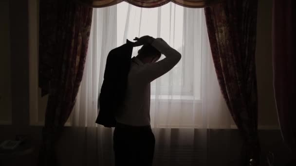 Man puts on black jacket standing before window. - Footage, Video
