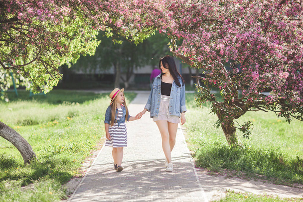 Young attractive mother and her little daughter having fun together on spring background. Girls in flowers. Family outdoors. Summer mood. - Photo, Image