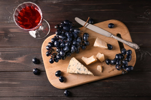 Copa de vino tinto con queso y uvas frescas sobre mesa de madera
 - Foto, imagen