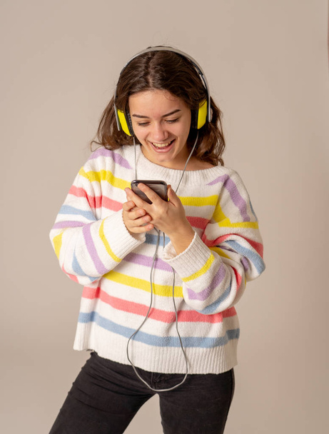 Portrait of gorgeous and happy teen woman listening to music in headphones looking for favorite song on mobile isolated on neutral. In positive emotions, youth, people, leisure and technology concept. - Fotografie, Obrázek