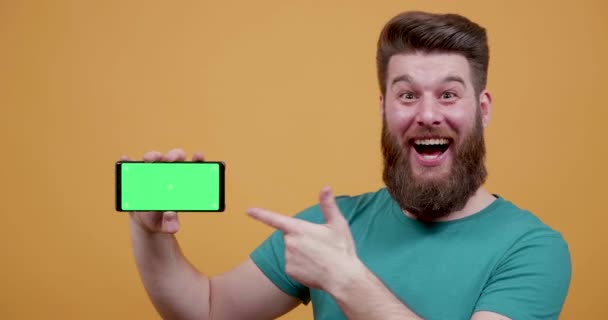 Very positive attractive young man point at his phones green screen - Video, Çekim