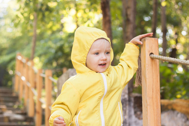 Divertente due anni ragazza in impermeabile giallo passeggiata nel parco nella giornata di sole
 - Foto, immagini