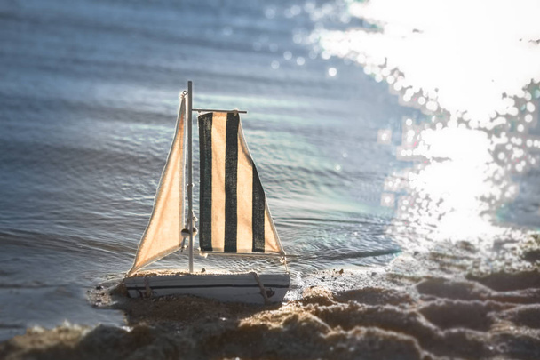  boat model toy ship near the sea on the beach on the sand lonely toy ready to big adventure  yacht for children sunny day  - Fotó, kép