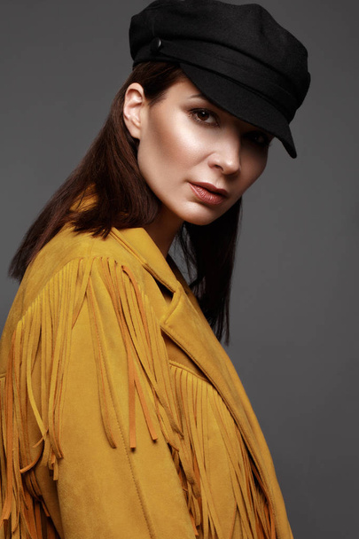 Beautiful girl with a classic make-up and a hairstyle in a fashionable designer jacket and cap, posing in the studio. Beauty face. - Zdjęcie, obraz
