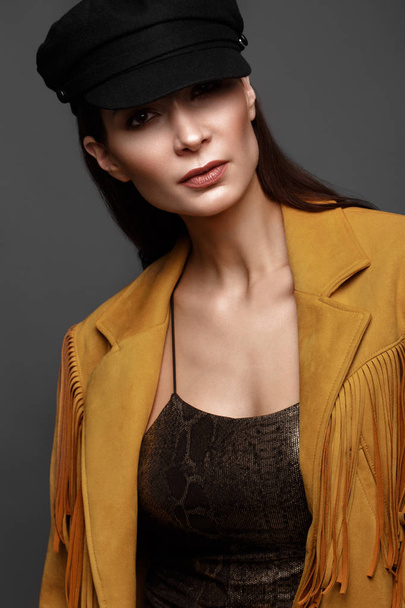 Beautiful girl with a classic make-up and a hairstyle in a fashionable designer jacket and cap, posing in the studio. Beauty face. - Foto, imagen