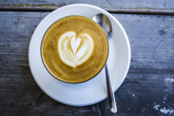 Dicke Glasbecher mit Cappuccino und Latte-Art in Herzform. frischen Kaffee mit Milch. auf einem Holztisch mit Untertasse, Löffel - Foto, Bild