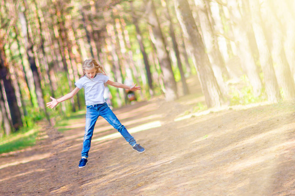 Little girl jumping outdoors in the forest. On the background of trees. - Fotografie, Obrázek