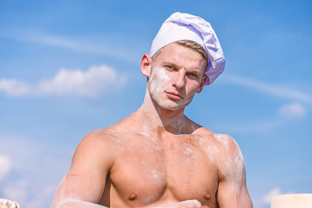 Chef in white hat on strict face, sky on background. Man with attractive appearance works as cook or baker, copy space. Sexy chef concept. Man with muscular torso covered with flour looks attractive - Photo, Image