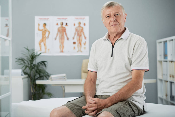 Portrét věku muže, který seděl na posteli v úřadu osteopat - Fotografie, Obrázek