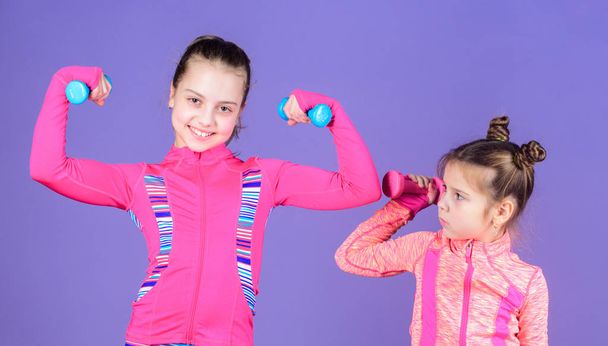 Girls cute kid exercising with dumbbells. Motivation and sport example concept. Toddler repeat exercise after sister. Sport exercises for kids. Healthy upbringing. Sporty babies. Following her sister - Photo, Image