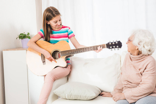Granddaughter playing on guitar for grandmother - Photo, Image