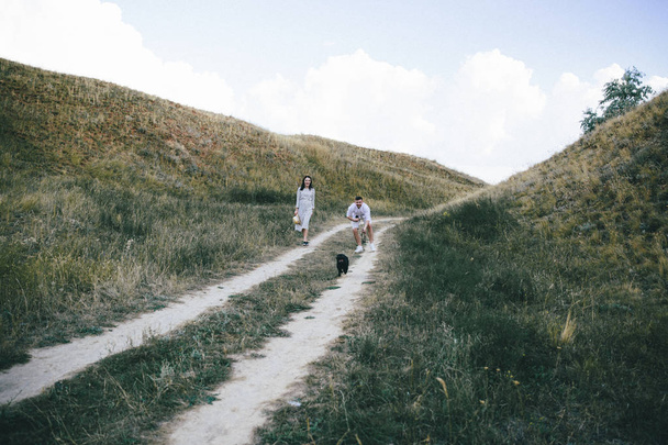 young couple with black french bulldog on hills on summer day - Zdjęcie, obraz