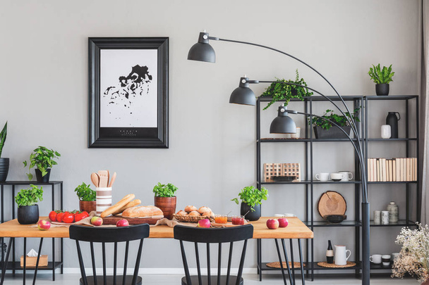 Real photo of an elegant daily room interior with a black shelf, lamp and dining table with herbs, bread and vegetables - Fotó, kép