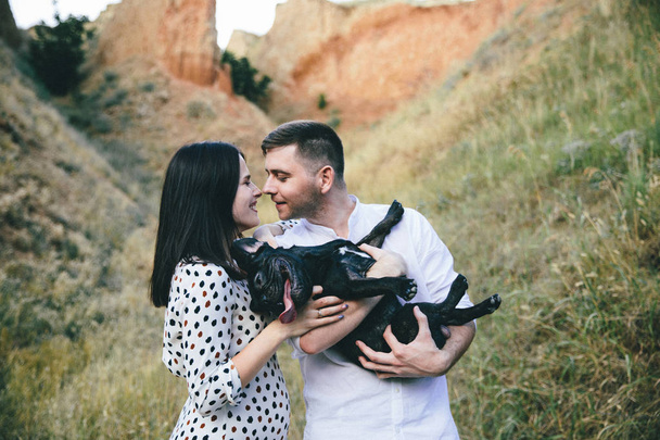 young couple with black french bulldog on hills on summer day - Photo, Image