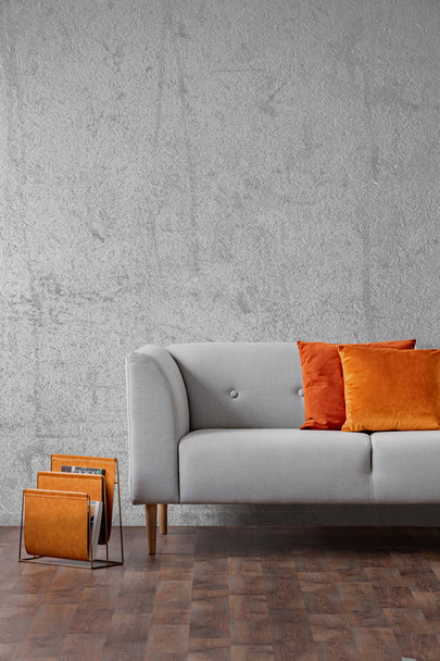 Orange pillows on grey settee in living room interior with concrete wall and wooden floor. Real photo - Photo, image