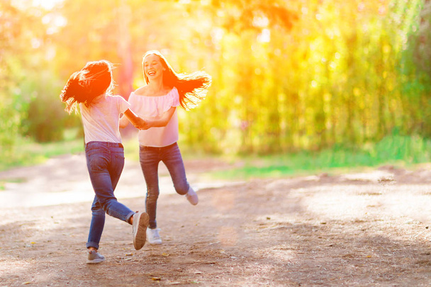 Two cheerful girlfriends whirl around holding hands in the woods. Summer sunny day. - Foto, afbeelding
