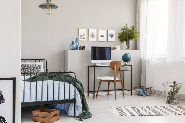 Wooden box under single metal bed with blue sheets and green blanket in trendy kid's room with workspace - Photo, image