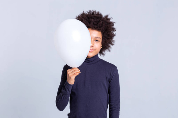 Pretty young man with afro hairstyle closing half of his face with balloon - Photo, image