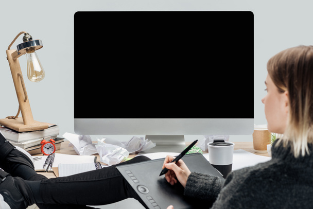 Mädchen sitzt am chaotischen Arbeitsplatz mit Beinen auf dem Schreibtisch und verwendet Grafik-Tablet isoliert auf grau - Foto, Bild
