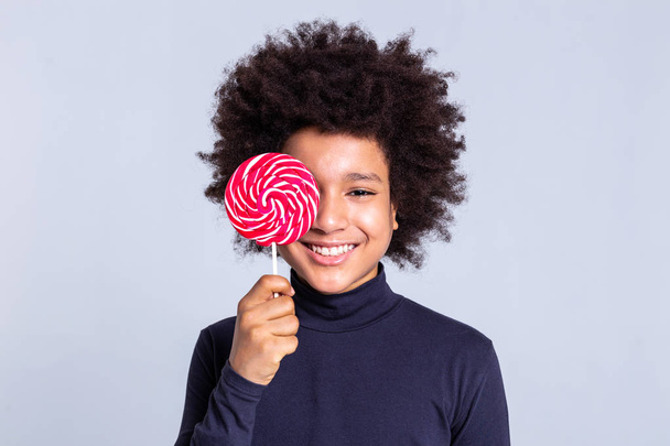 Alegre niño afroamericano con el pelo salvaje cubriendo la cara con grandes dulces
 - Foto, imagen