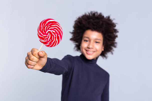 Resolute dark-haired joyful boy pulling out hand with candy in it - Φωτογραφία, εικόνα
