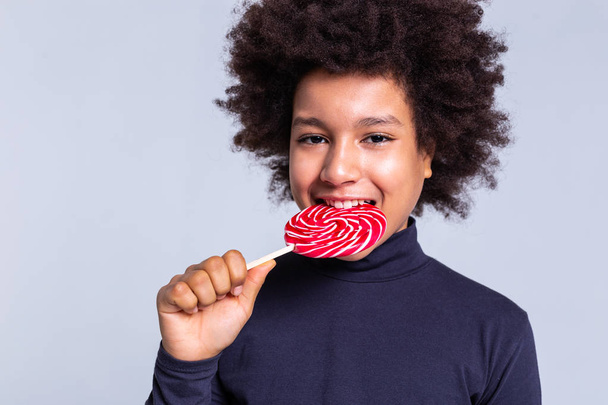 Cheerful African American child biting red sticky candy - Foto, immagini