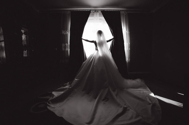 Sylwetka piękna panna młoda w domu. Stanowisko pracy szwaczki przez okno w sukni ślubnej. Czarno-białe - Zdjęcie, obraz