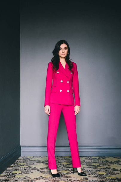 young stylish woman in pink suit posing in dark room with grey walls - Фото, зображення