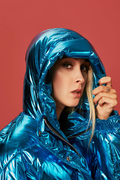 Blond štíhlá dívka v modrém péřová bunda pokrývá její tvář od větru s kapucí - Fotografie, Obrázek
