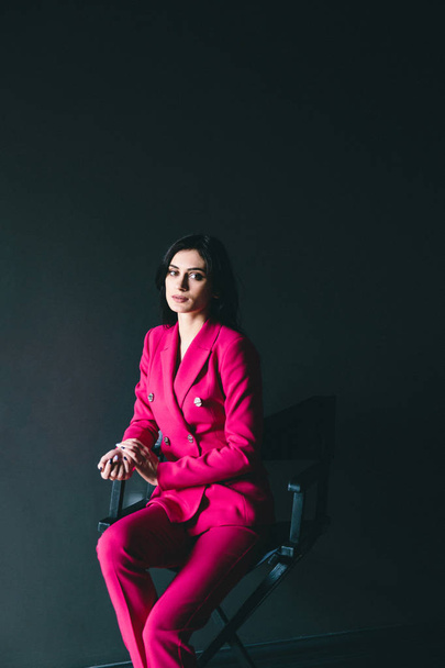 young stylish woman in pink suit posing in dark room with grey walls - Foto, immagini